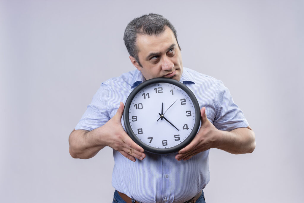 middle-aged man in blue vertical striped shirt holding wall clock in hands thoughtful about confusing idea on a white background